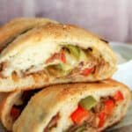 Tasty stuffed sandwich with meat, cheese, and peppers on a wooden surface.