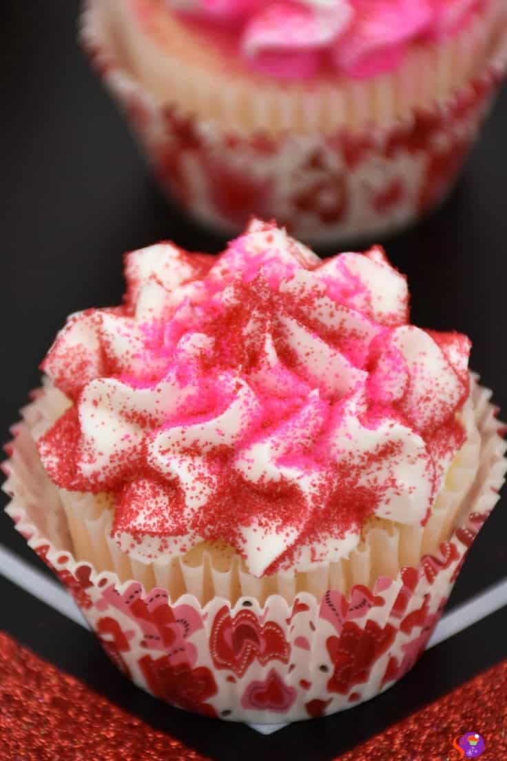 Valentine's Cupcakes with pink sprinkles on a cream frosting, displayed with a heart-themed wrapper.