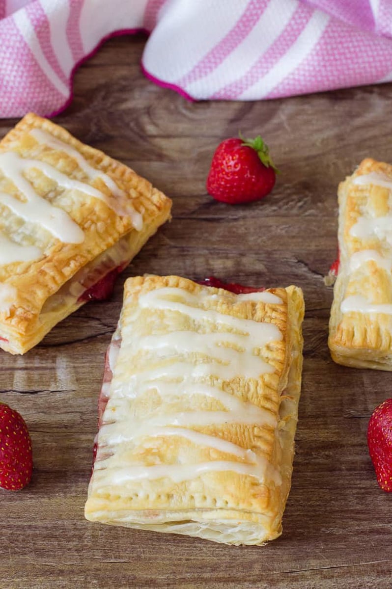 Puff pastry strawberry strudel on wooden table with strawberries.