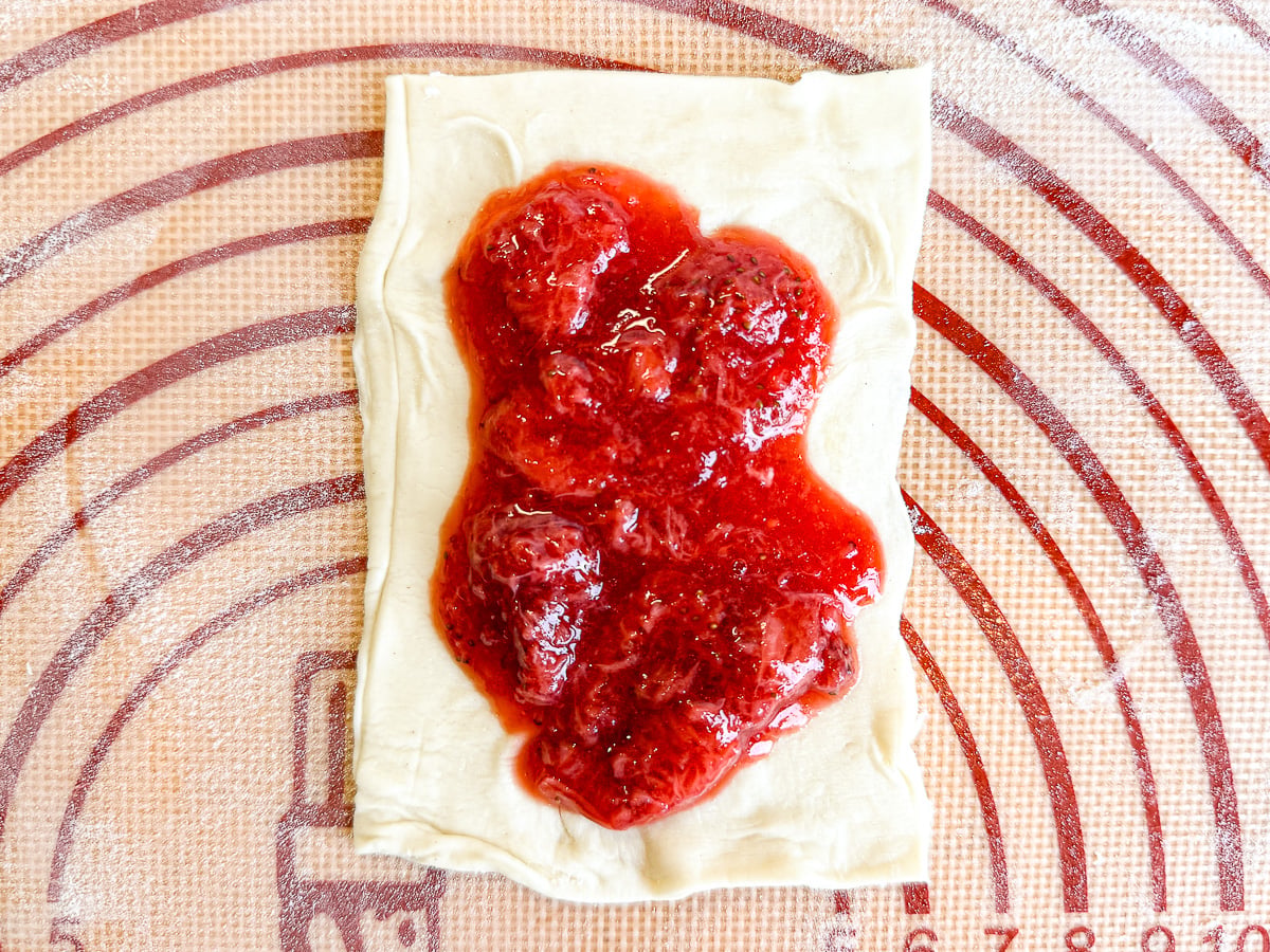 Strawberry filling in puff pastry square on table.