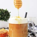 Honey drizzling onto a frothy cup of a Toasted Coconut Honey Latte with a backdrop of a light, bright kitchen setting.