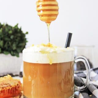 Honey drizzling onto a frothy cup of a Toasted Coconut Honey Latte with a backdrop of a light, bright kitchen setting.