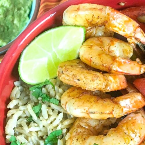 Savor the Shrimp Fajita Bowls: a delightful mix of spiced shrimp and sliced bell peppers, served with brown rice, lime wedges, and a side of creamy guacamole.