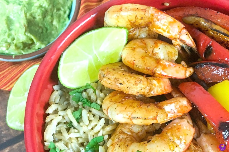 Savor the Shrimp Fajita Bowls: a delightful mix of spiced shrimp and sliced bell peppers, served with brown rice, lime wedges, and a side of creamy guacamole.