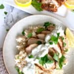 Grilled Greek chicken served over rice with a dollop of tzatziki sauce, garnished with parsley and a side of lemon slices.