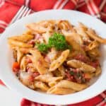 A plate of Instant Pot penne pasta with tomato sauce and parsley on a red and white checkered napkin.