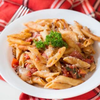 A plate of Instant Pot penne pasta with tomato sauce and parsley on a red and white checkered napkin.