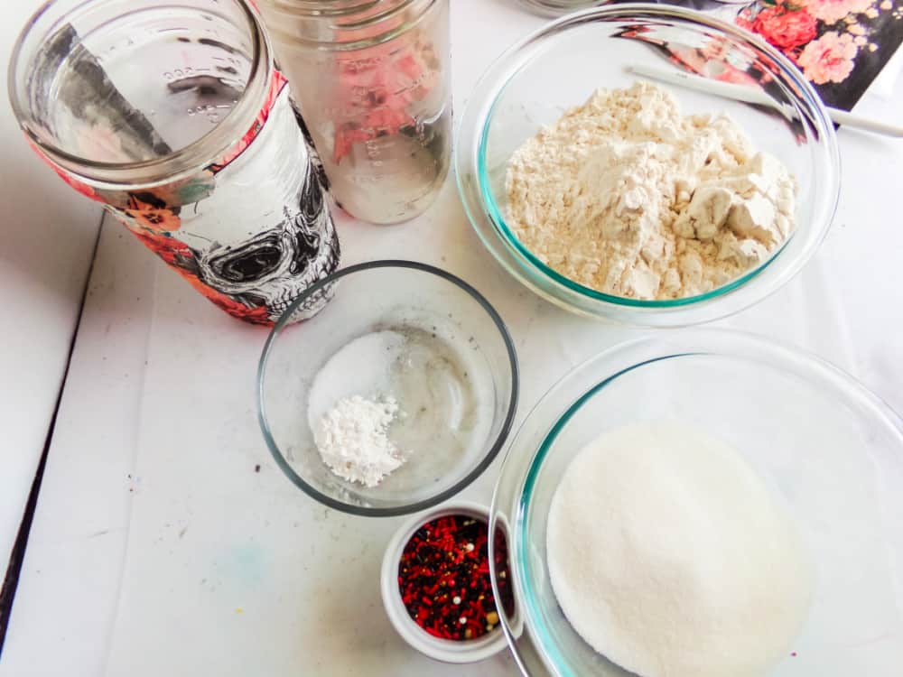 A hand adjusts a gray cloth cover tied with a black ribbon on the Skull Cookie Mix in a Jar, adorned with an eerie black skull design.