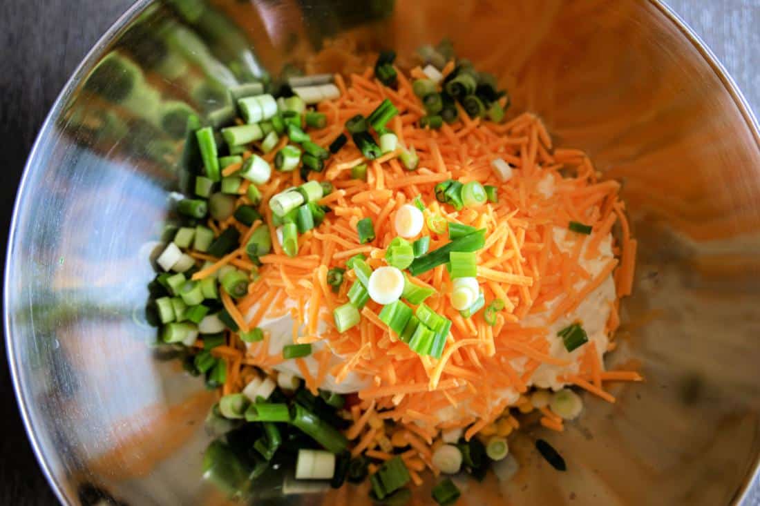 Shredded carrots and chopped green onions in a stainless steel mixing bowl for Southwestern Corn Dip.