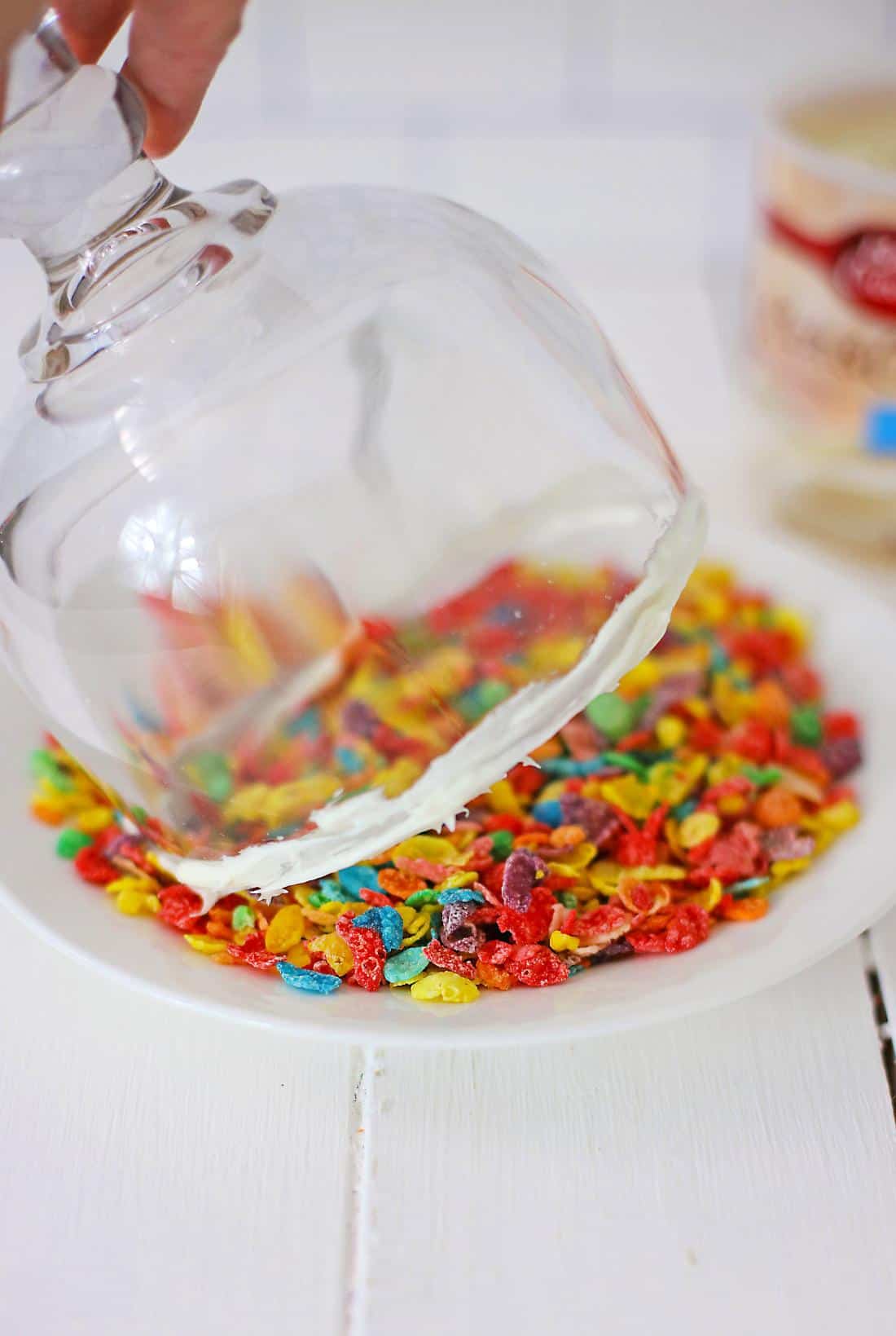 A jar of colorful Fruity Pebbles being spilled onto a white surface.