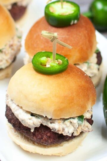 Air fryer jalapeno popper burger sliders on plate next to jalapeno peppers.