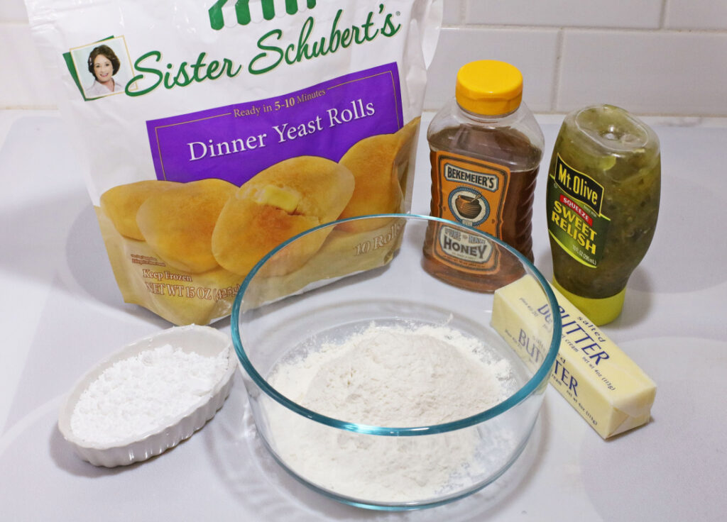 Copy Cat Chick-Fil-A Chicken Mini's 3 Ingredients for a delicious spread, including Sister Schubert's dinner rolls and all the fixings for Chick-Fil-A Chicken Minis, such as honey, sweet relish, butter, flour, and powdered sugar, are neatly arranged on the counter.