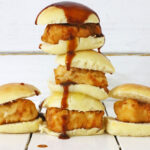 A stack of Chick-Fil-A Mini's, with barbecue sauce gently dripping, rests invitingly on a white wooden surface.
