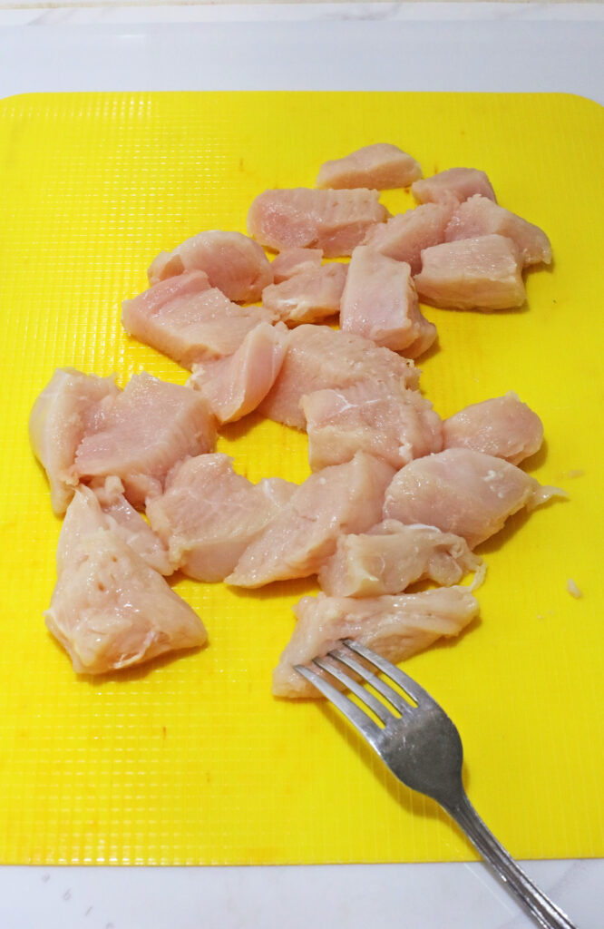Copy Cat Chick-Fil-A Chicken Mini's 6 Raw chicken pieces on a yellow cutting board with a fork in the foreground, evoking the first step in preparing delicious homemade Chicken Minis.