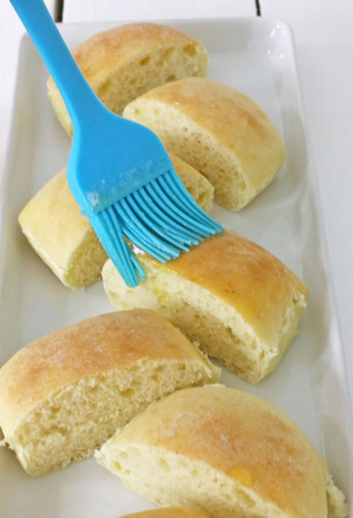 Copy Cat Chick-Fil-A Chicken Mini's 9 A blue brush delicately applies butter to freshly baked bread rolls, reminiscent of Chick-Fil-A Chicken Minis, on a rectangular white plate.