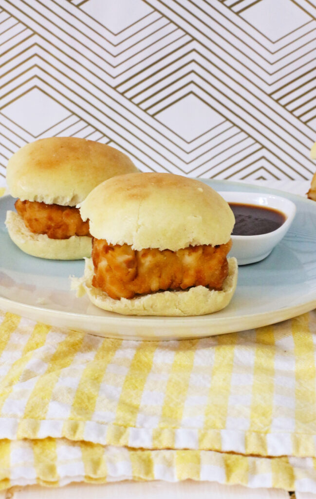 Copy Cat Chick-Fil-A Chicken Mini's 11 Two delicious Chicken Minis sit on a plate, accompanied by a bowl of dipping sauce in the background, all beautifully arranged on a yellow and white striped cloth.