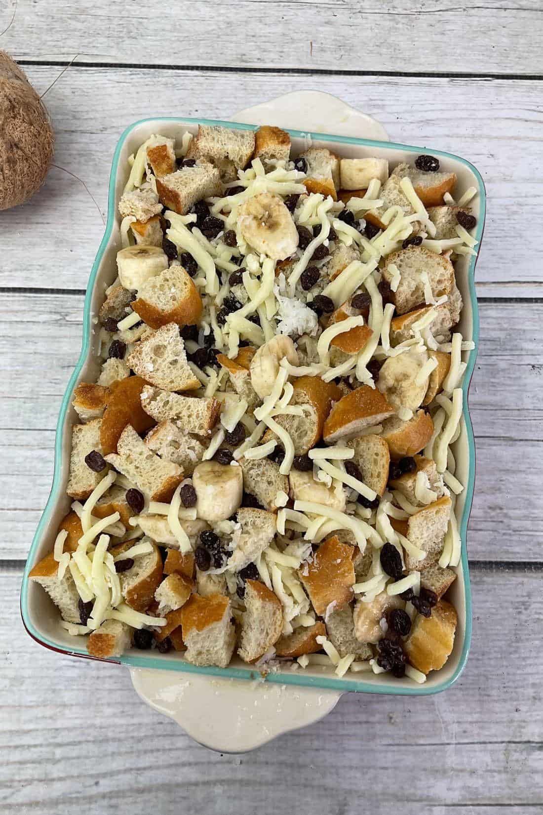 Mexican unbaked bread pudding mixture with bananas, raisins, and shredded cheese in a baking dish.