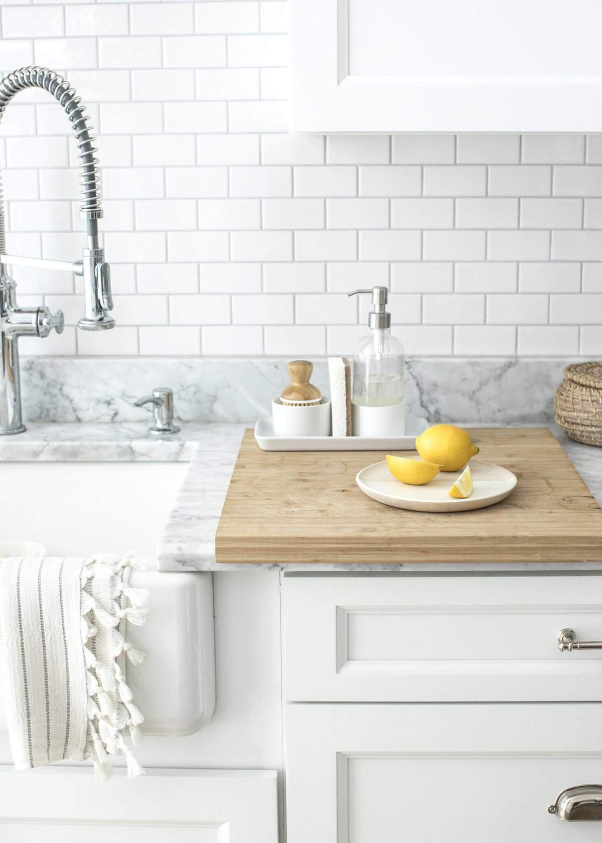 Modern kitchen countertop with white cabinetry, marble backsplash, and stainless-steel faucet, adorned with a cutting board, lemons, and hand soap.