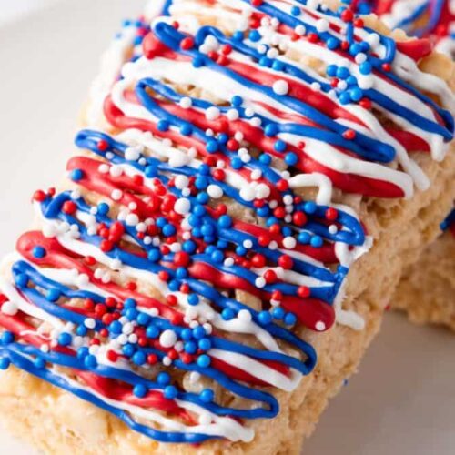 These Independence Rice Krispie Treats are adorned with vibrant red, white, and blue icing and sprinkles, elegantly displayed on a pristine white surface.
