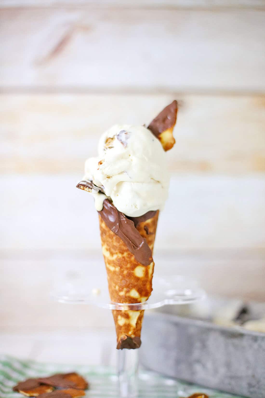 A hand dips a folded crepe into a dish of thick chocolate sauce with a spoon on the side, reminiscent of indulgent flavors found in Ben & Jerry's Copycat No Churn Homemade Americone Dream Ice Cream.