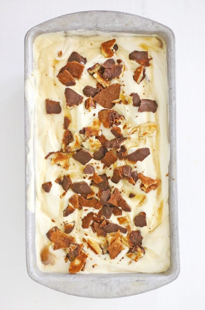 A rectangular metal container brims with creamy vanilla ice cream, lavishly topped with brown cookie or chocolate pieces, capturing the essence of Ben & Jerry's Copycat No Churn Homemade Americone Dream Ice Cream.