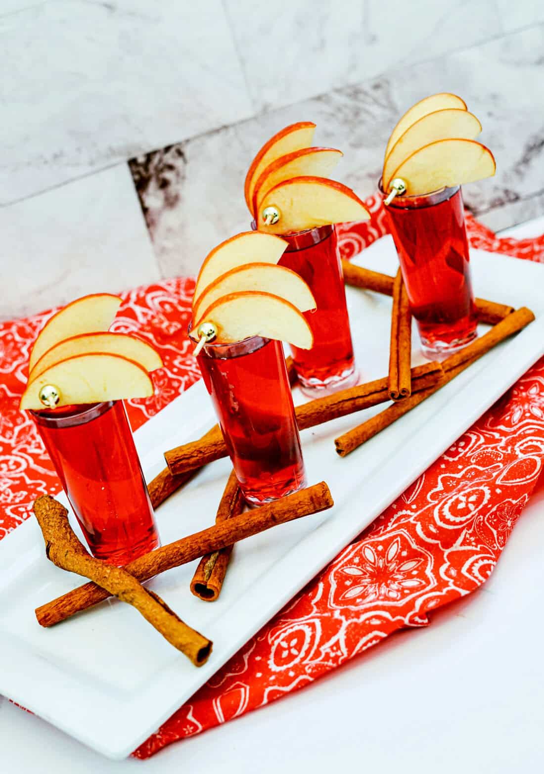 Cranberry juice, two apples, and a bottle of Crown Royal Apple whiskey sit elegantly on a marble surface, accompanied by a green Crown Royal bag. This setup hints at the perfect Cran Apple experience or crafting a delightful Crown Cran Apple Shooter.