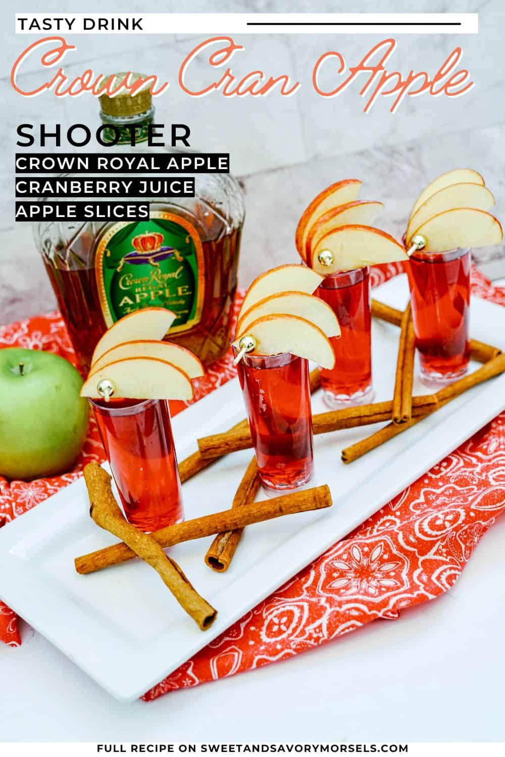 Apple slices and a knife rest on a cutting board beside a Crown Cran Apple Shooter whiskey bottle and a green bag, with a whole apple on a marble surface.