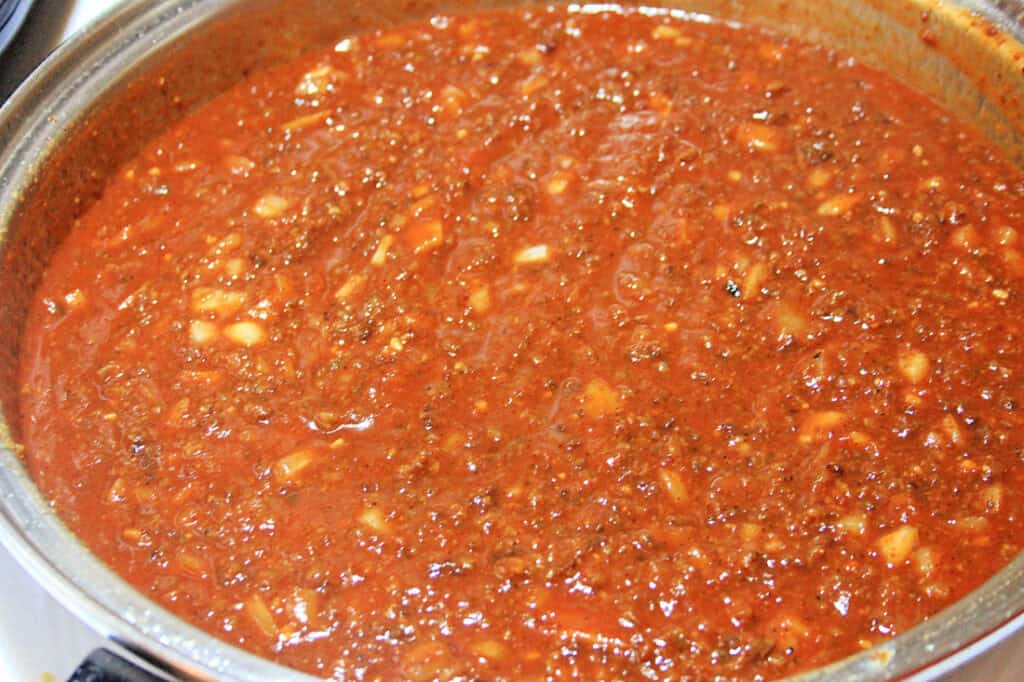 Close-up of a large pot filled with chunky tomato sauce, containing visible pieces of chopped onions and herbs, perfect for topping chili cheese baked potatoes.