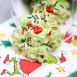 Green candy clusters with colorful sprinkles and heart decorations, all set on a festive napkin featuring a cartoon character in a Santa suit. These whimsical treats, dubbed Grinch Poop Peanut Clusters, add a fun and playful touch to your holiday celebrations.