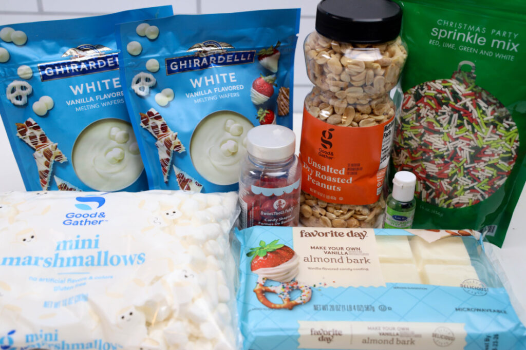 Assorted baking supplies, perfect for making Grinch Poop Peanut Clusters, include vanilla melting wafers, marshmallows, roasted peanuts, almond bark, sprinkles, and food coloring all neatly arranged on the countertop.