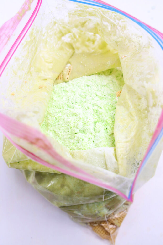 An open plastic bag reveals a light green powder, reminiscent of Grinch Puppy Chow, spread on a white surface.