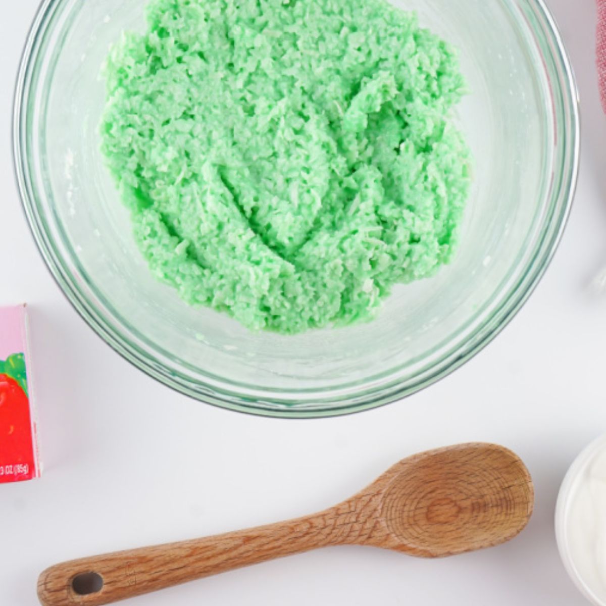 Yogurt, green Jell-o and coconut flakes mixed together in a glass bowl.