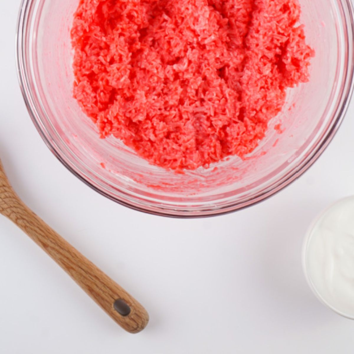 Yogurt, red Jello, coconut flakes combined in a glass bowl.
