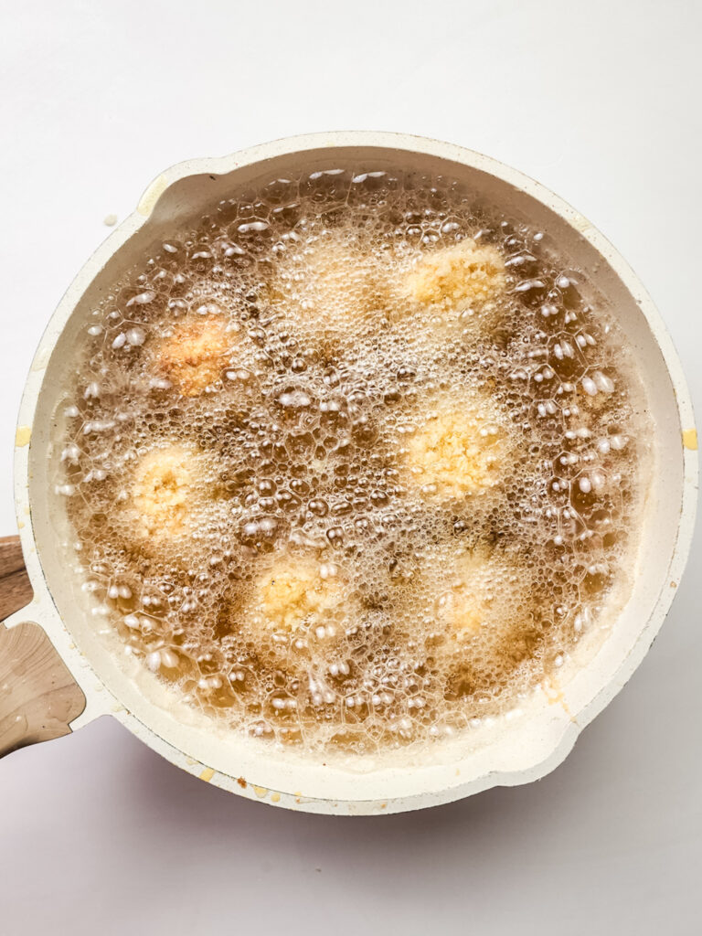 Frying pan with oil sizzles as deep-fried mac and cheese bites bubble at the surface, creating a mouthwatering aroma.