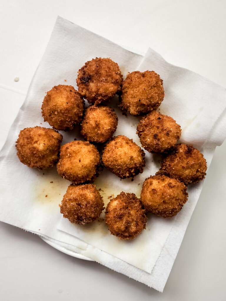 Golden brown fried Mac and Cheese Bites are arranged on a white paper towel, perfectly placed on a plate.