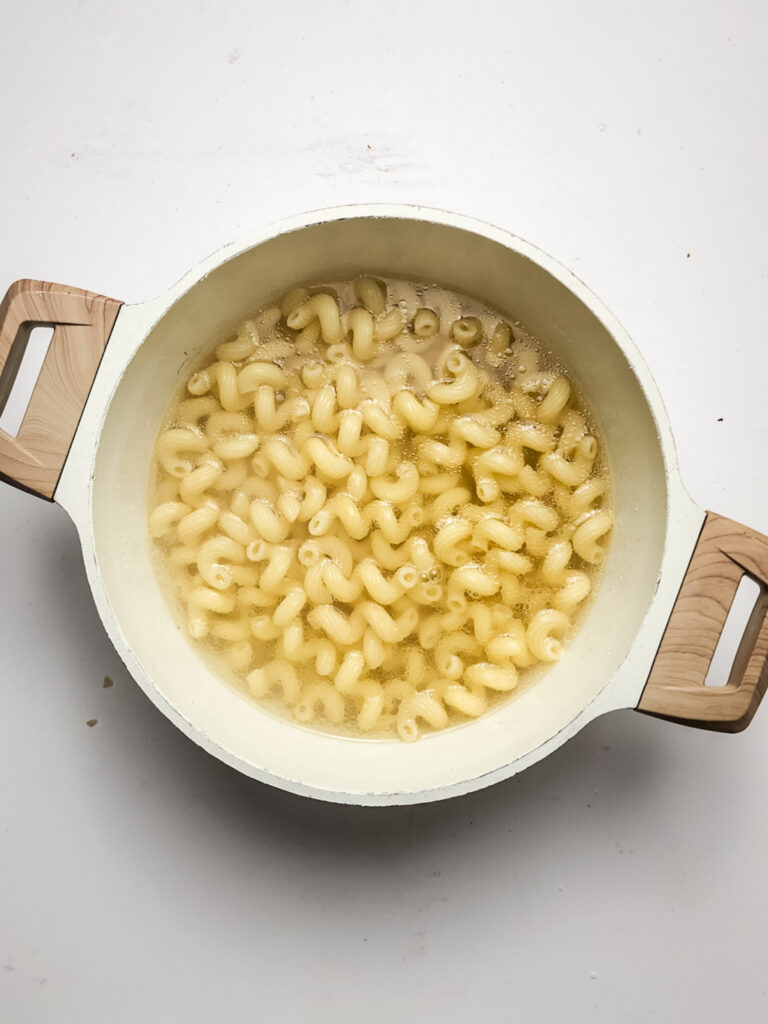 A white pot with wooden handles is filled with cavatappi pasta in boiling water, viewed from above, ready to be transformed into delicious fried mac and cheese bites.