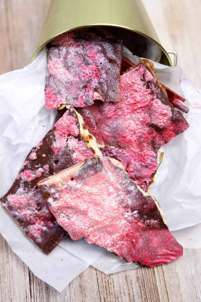 Glitter Valentine's Cracker Candy: A Sweet & Sparkly Treat 12 Crimson-colored chocolate bark with a dusting of white sprinkles, reminiscent of Glitter Valentine's Cracker Candy, partially spills out of a metal container onto white parchment paper.