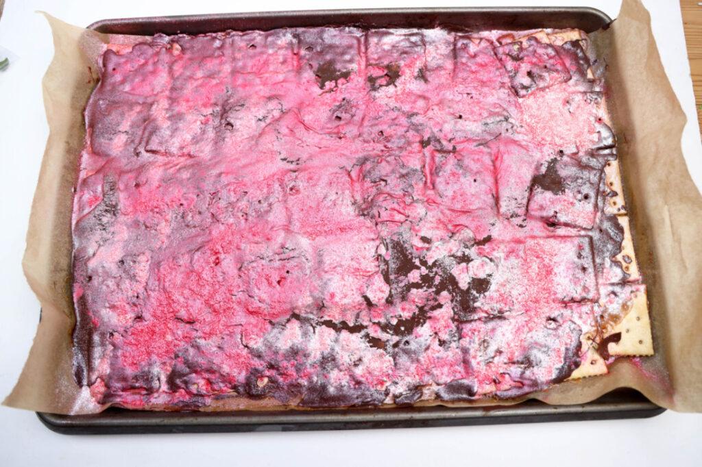 Glitter Valentine's Cracker Candy: A Sweet & Sparkly Treat 9 A baking tray holds a rectangular cake, its uneven, shiny pink icing reminiscent of Glitter Valentine's Cracker Candy. The cake rests elegantly on parchment paper.