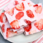 Plates with strawberry frozen yogurt bark squares sit on a striped cloth background.