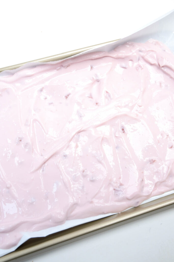 A baking tray lined with white paper is filled with velvety pink cake batter, reminiscent of strawberry frozen yogurt bark.