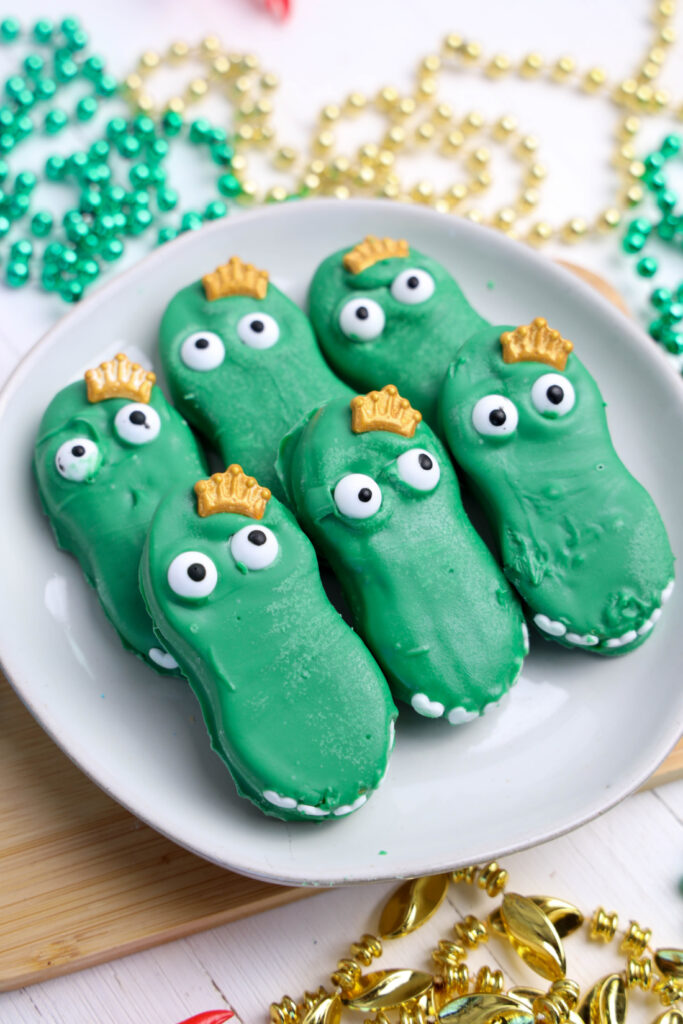 Easy Mardi Gras Alligator Cookies (No-Bake) 9 A plate of six enchanting Mardi Gras Alligator Cookies, each with googly eyes and tiny golden crown decorations, surrounded by festive beads.