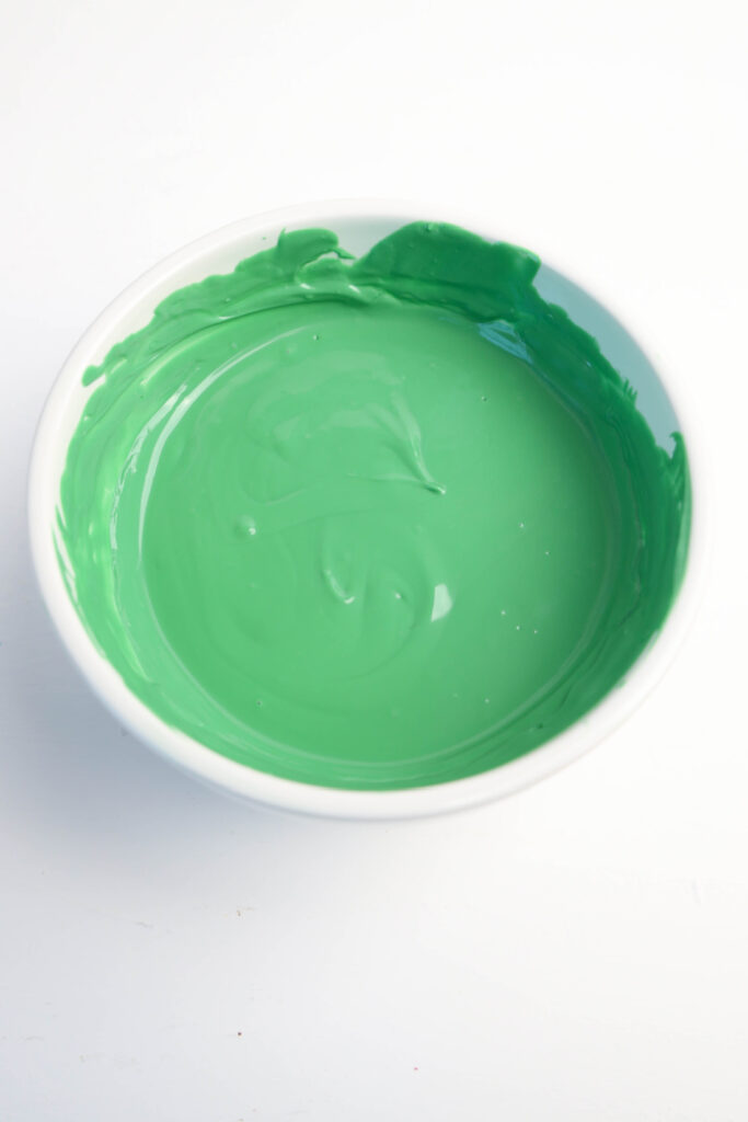 Easy Mardi Gras Alligator Cookies (No-Bake) 5 A white bowl filled with smooth, green paint sits on a white surface, reminiscent of the vibrant hues used to decorate festive Mardi Gras Alligator Cookies.