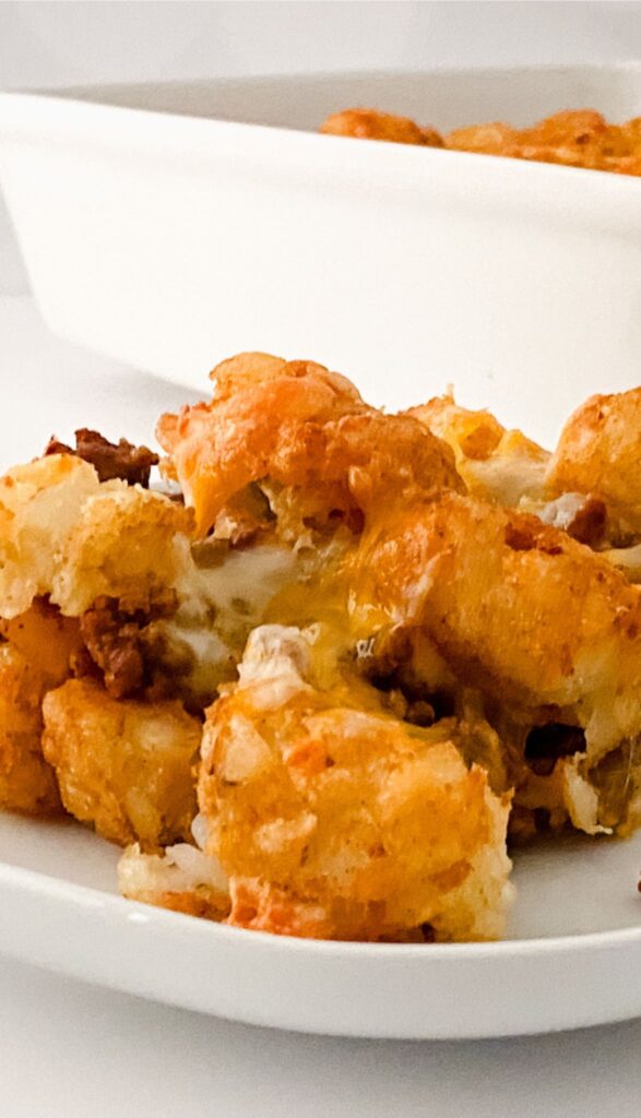 Close-up of a plate with a portion of Tasty Taco Tot Casserole, featuring crispy tater tots and melted cheese. A baking dish is visible in the background.