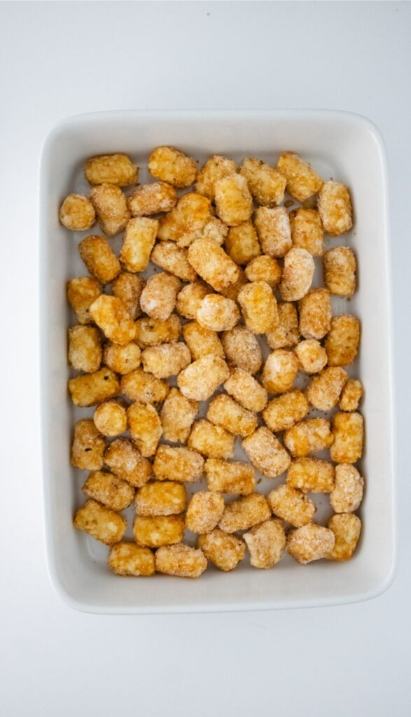 A white rectangular dish filled with half of the baked golden-brown tater tots, reminiscent of a Taco Tot Casserole.