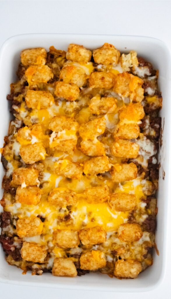 A delicious Taco Tot Casserole features a grid of golden tater tots atop layers of melted cheese and savory ground meat, all baked to perfection in a white rectangular dish.