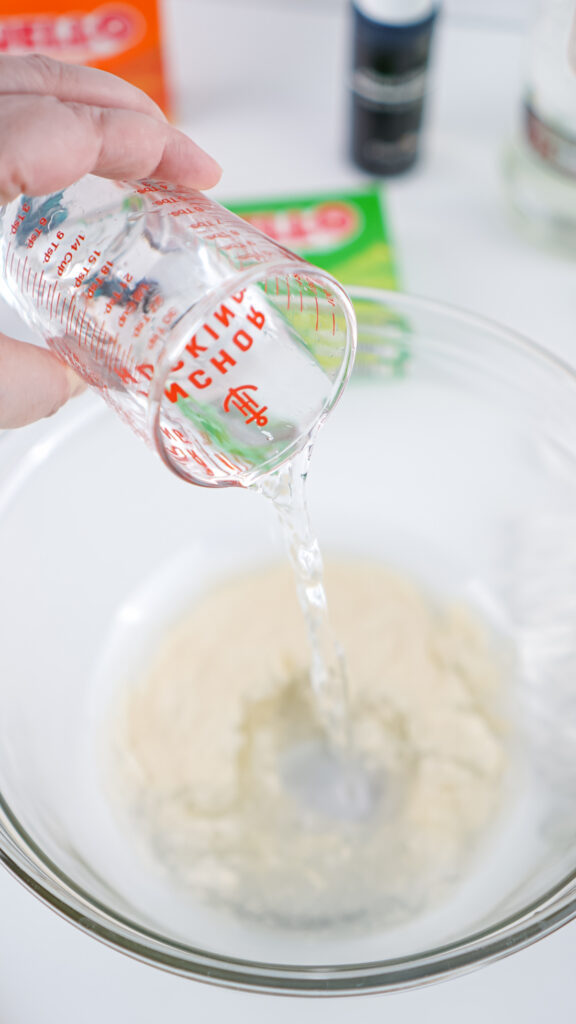 Eagles Jello Shots 5 A hand pours clear liquid from a measuring cup into a bowl with dry ingredients, setting the stage for some festive jello shots.