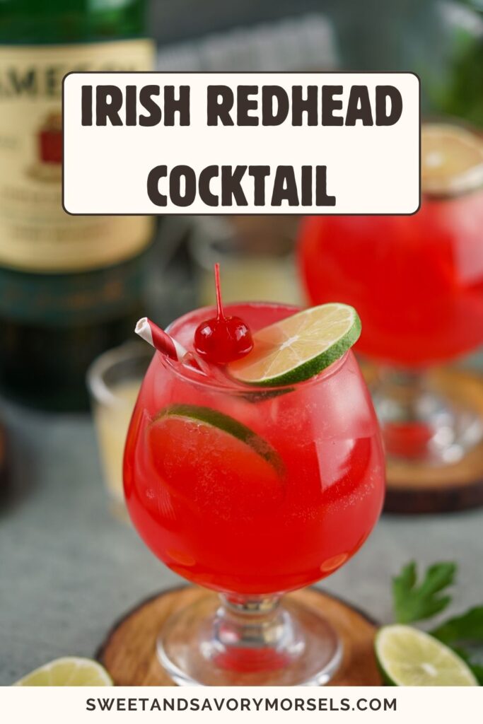 A vibrant red cocktail in a round glass, garnished with a lime slice and a cherry on top. In the background, a bottle features the text "Irish Redhead," adding a touch of allure to this delightful Irish Redhead Cocktail.