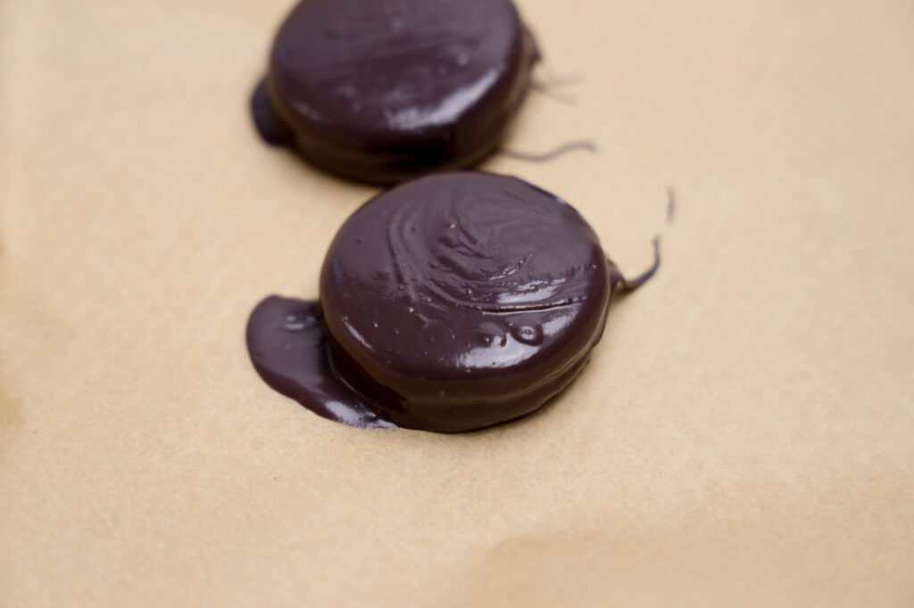 Two round Summerween Slasher Oreos rest on a sheet of brown parchment paper, with some chocolate pooled around the edges.