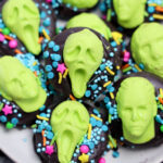 Plate of Summerween Slasher Oreos—chocolate cookies decorated with bright green candy faces, some screaming, and topped with colorful sprinkles.