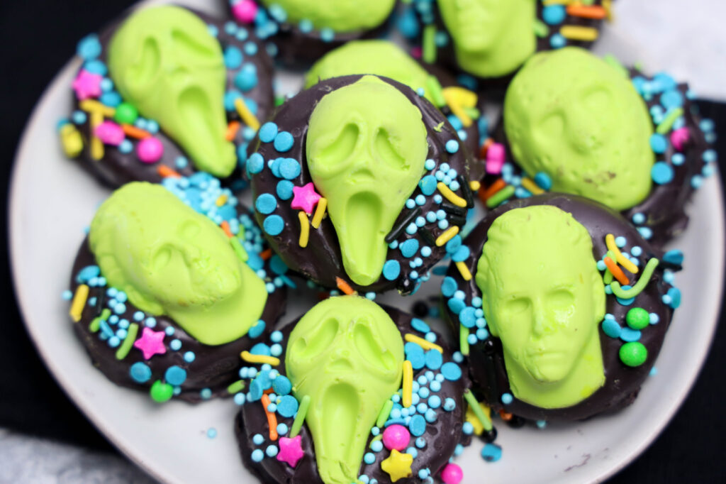 A plate of Summerween Slasher Oreos topped with neon green faces and decorated with colorful sprinkles.